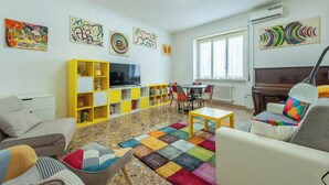 Een woonkamer met een bank, fauteuils, een salontafel, een televisie, een boekenkast en kunstwerken aan de muur.