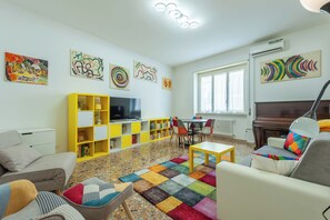 A living room with a sofa, armchairs, a coffee table, a TV, a bookshelf, and artwork on the walls. - Bright & Stylish Flat near Villa Pamphili (Roma)
