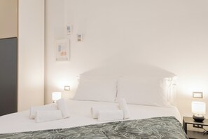 Ein ordentlich gemachtes Bett mit weißen Laken, einem grün gemusterten Überwurf und zwei Nachttischlampen.