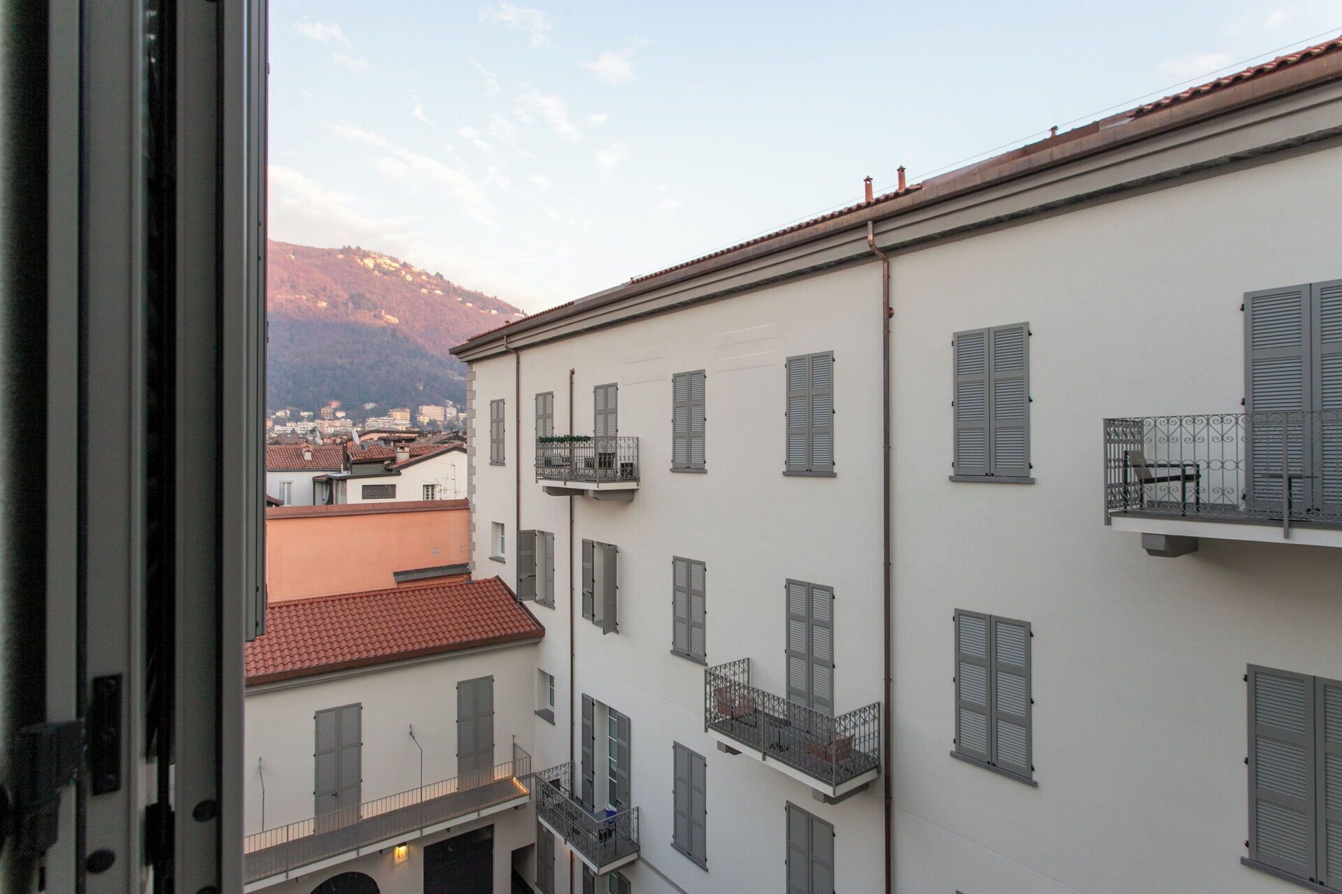 A multi-story building with balconies, a red-tiled roof, and a mountain in the background.