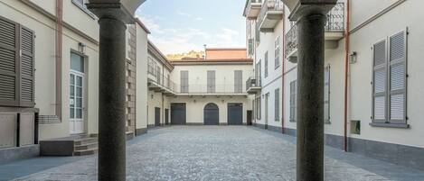 Un patio abierto con columnas de piedra, suelo adoquinado y edificios con contraventanas y balcones.