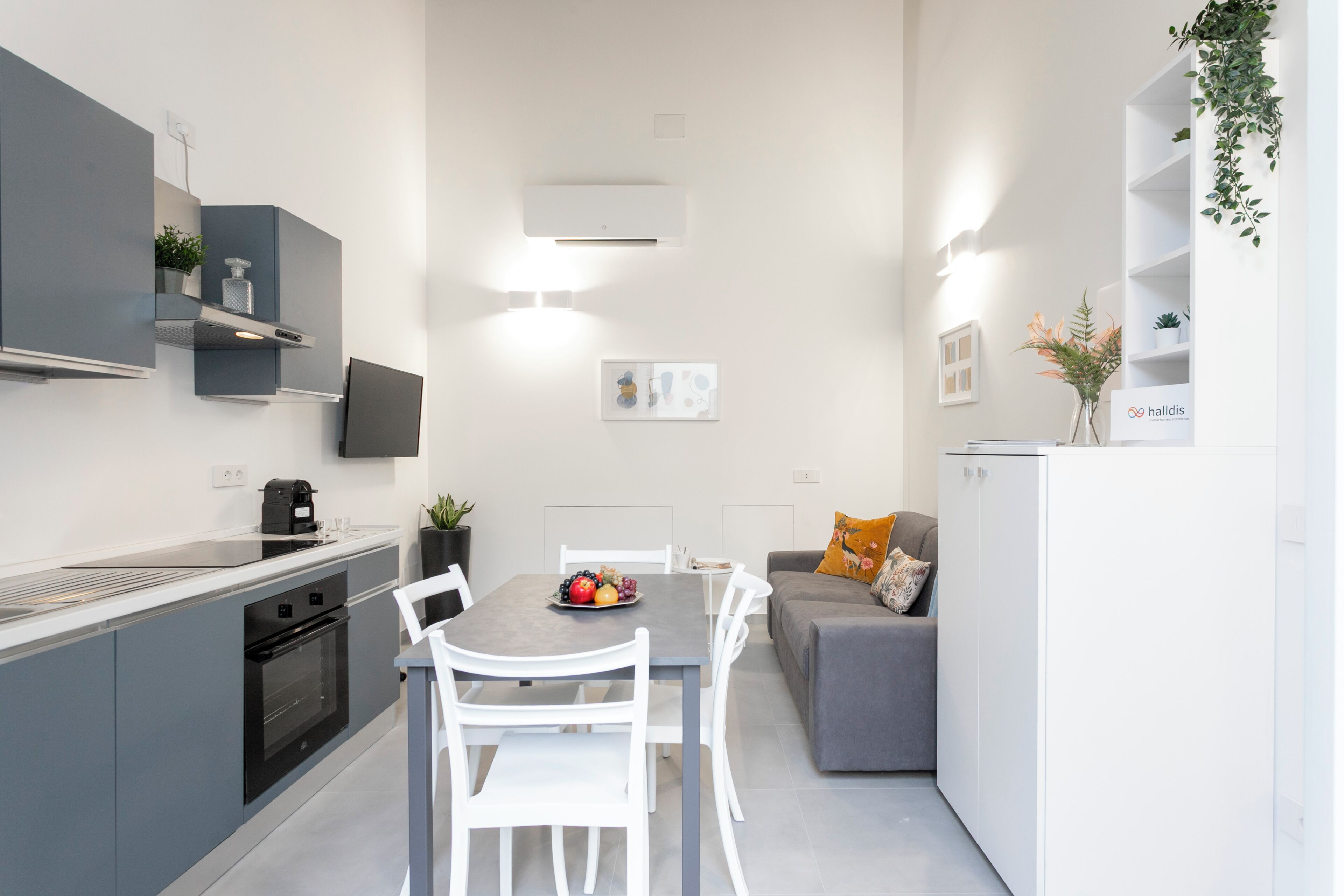 A modern kitchen with white cabinets, a grey countertop, and a dining area with a grey sofa and white chairs.