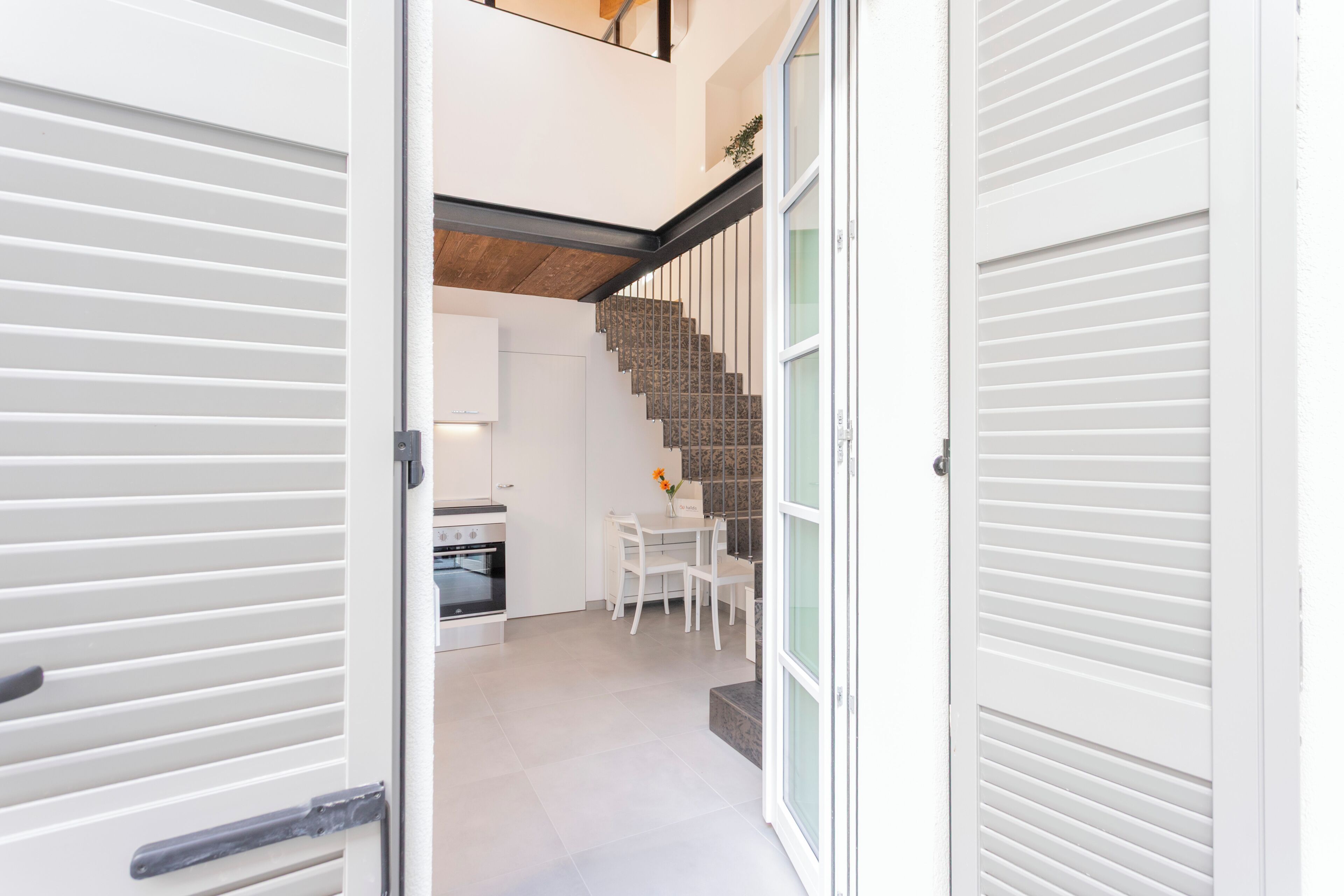 Een moderne keuken met witte kasten, een eethoek met een witte tafel en stoelen, en een trap met een houten afwerking.