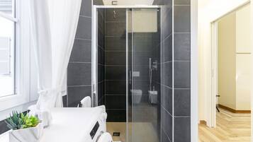 Un bagno moderno con cabina doccia in vetro, pareti piastrellate di colore scuro e un lavandino bianco.