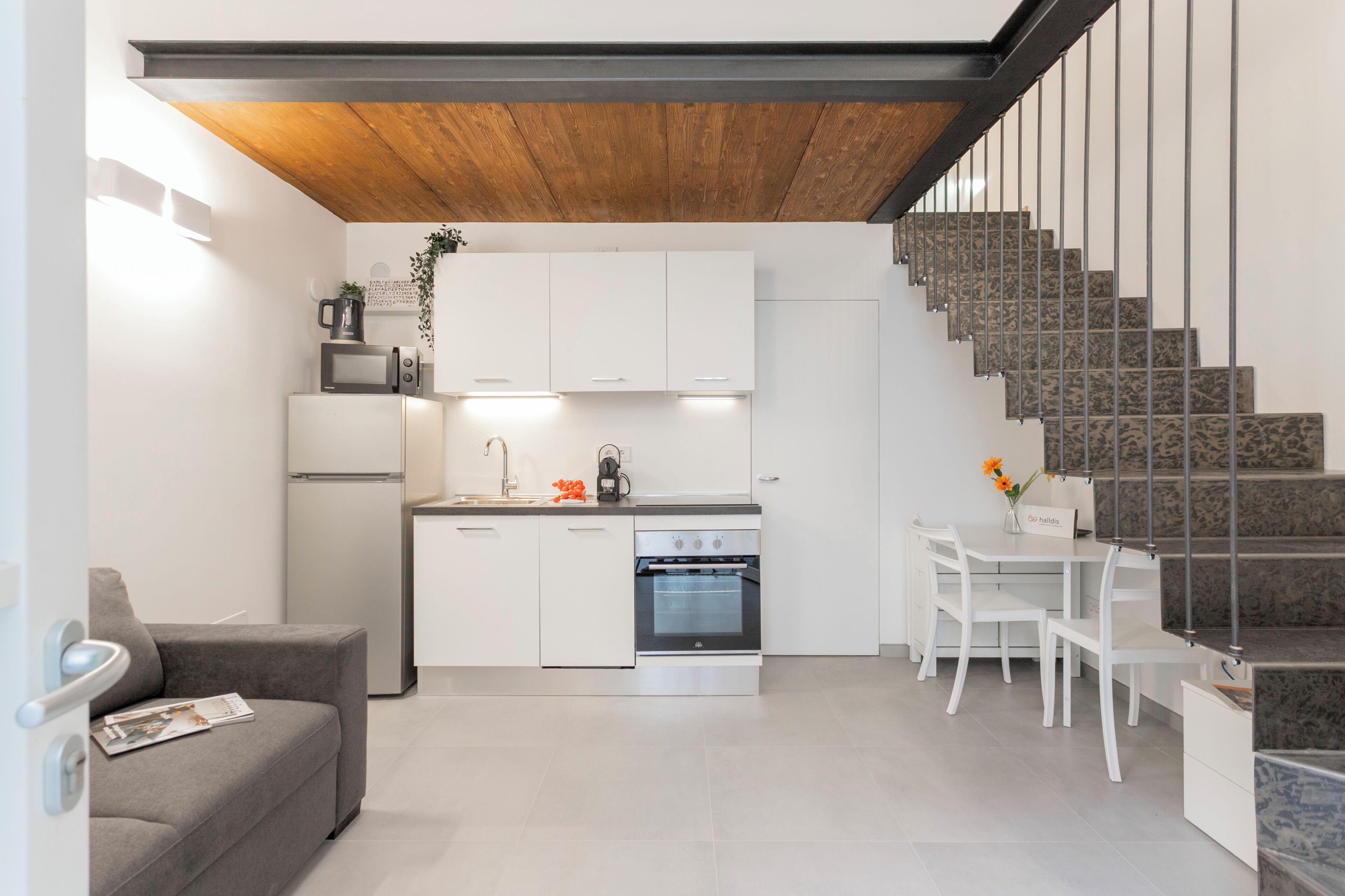 A modern kitchen with white cabinets, a built-in oven, and a dining area with white chairs.