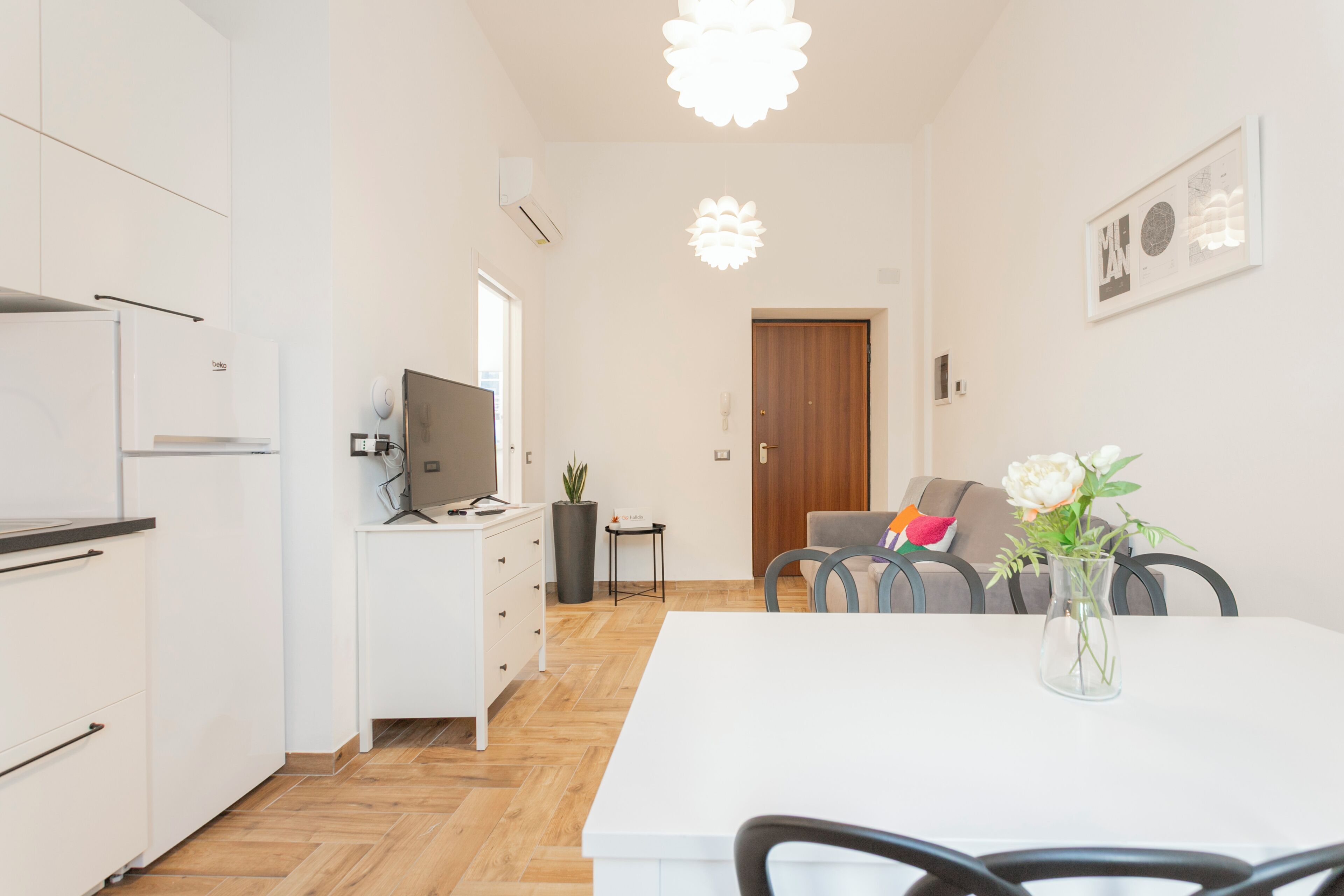 A modern kitchen with white cabinets, a dining area with a white table, and a living space with a sofa and a vase of flowers.