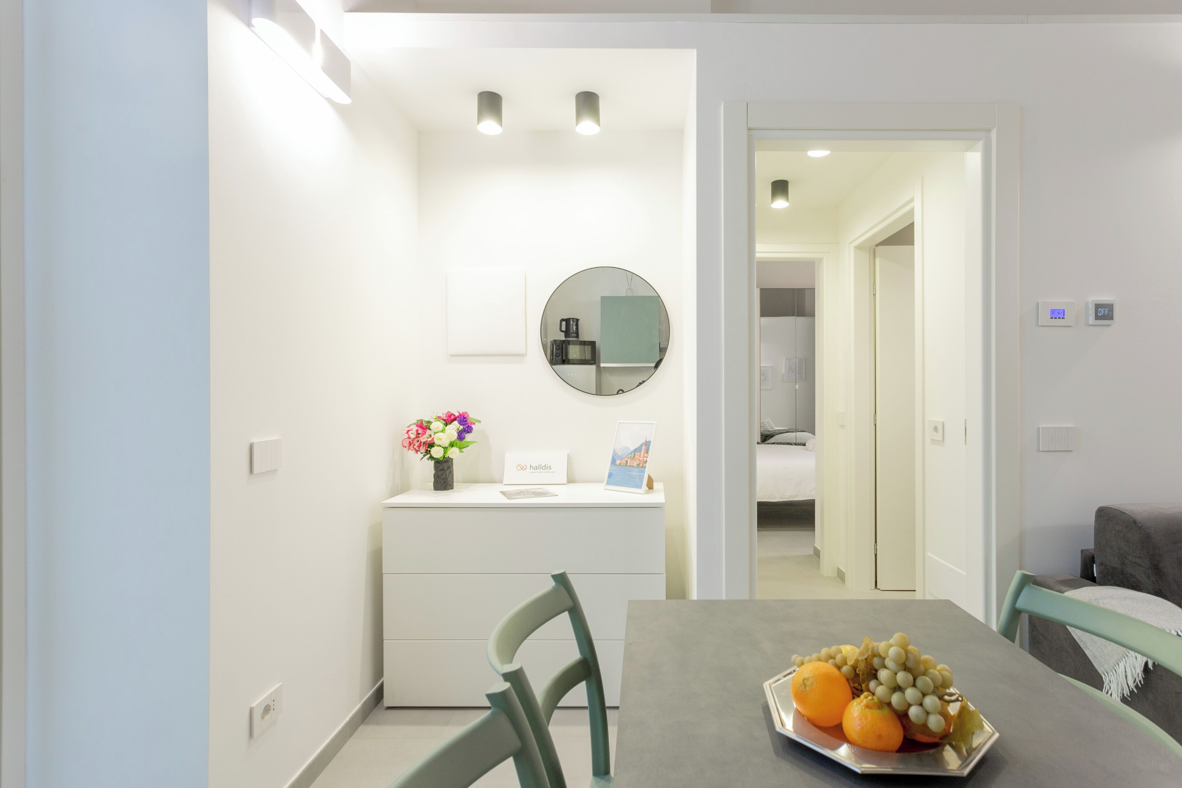 A modern room with a dining table, chairs, a small counter with a mirror, and a wall-mounted light fixture.