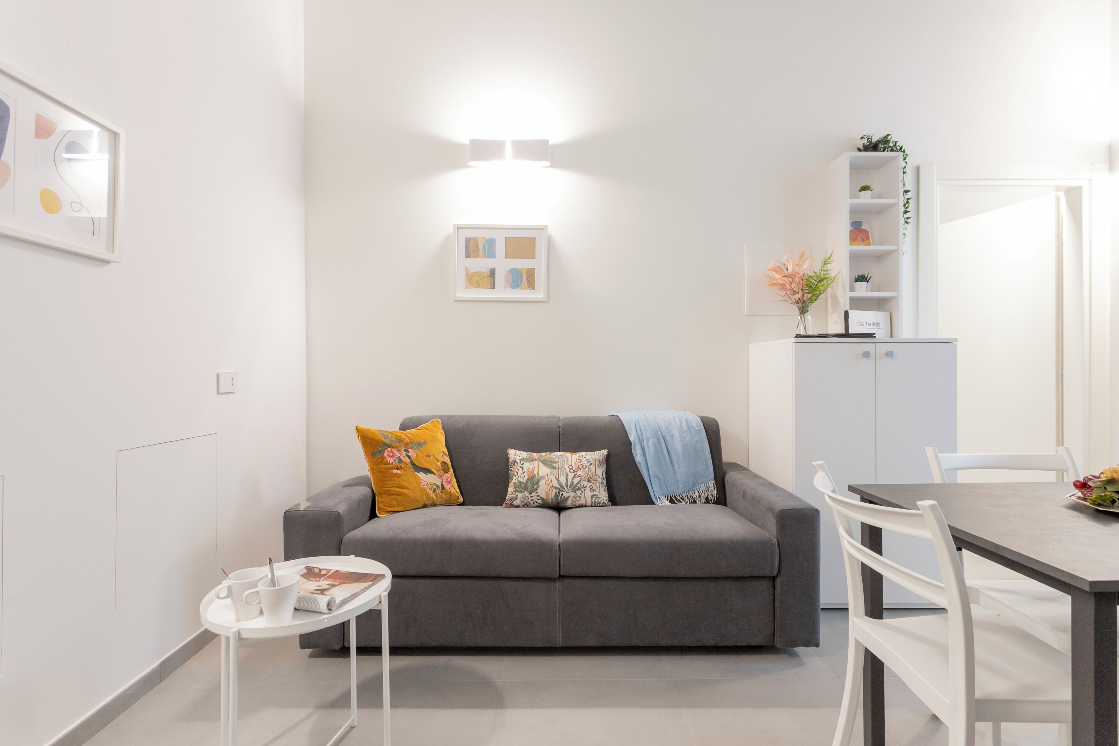 Una sala de estar moderna con un sofá gris, una mesita blanca y una zona de comedor con una mesa y sillas blancas.