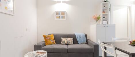 Una sala de estar moderna con un sofá gris, una mesita blanca y una zona de comedor con una mesa y sillas blancas.