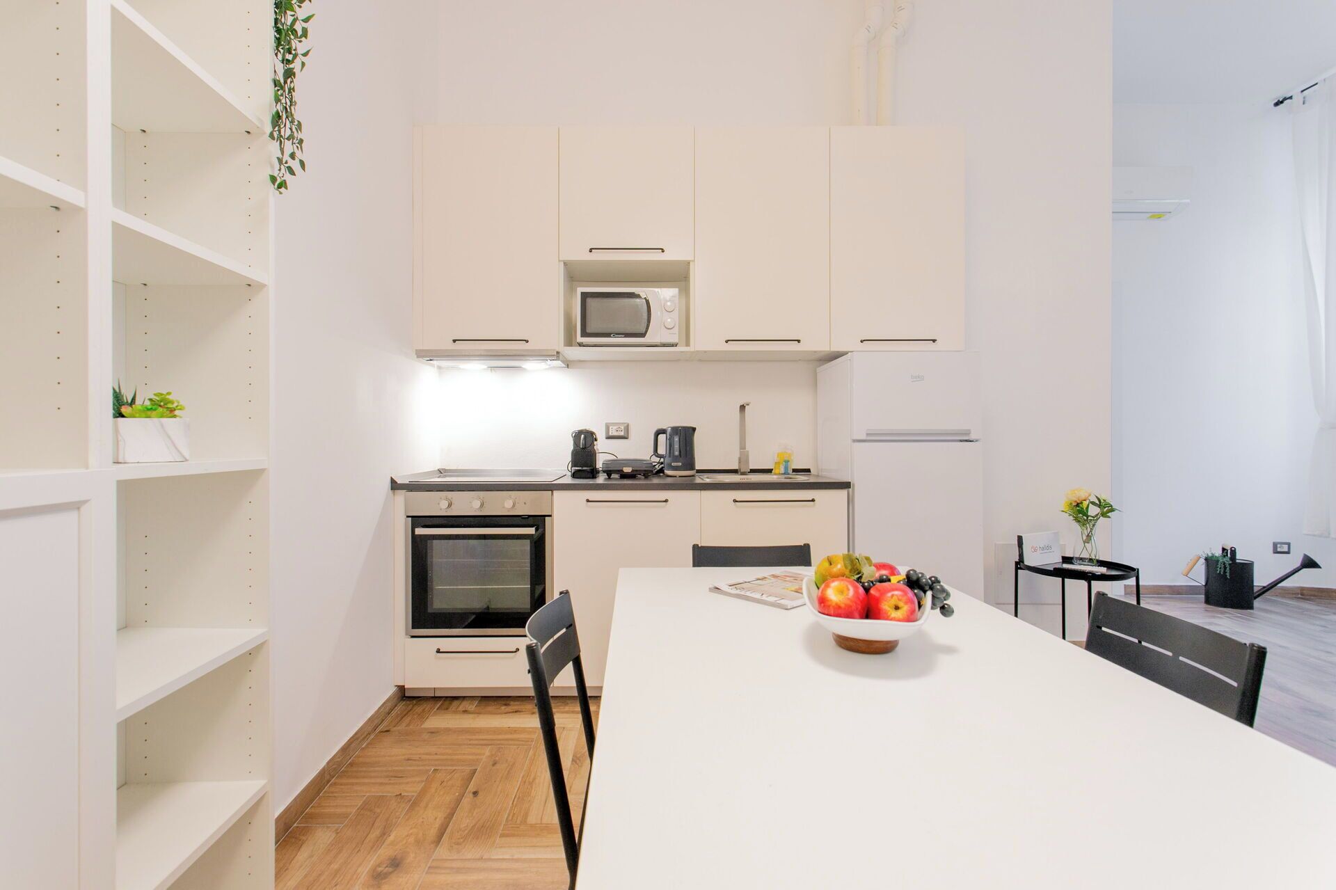 A modern kitchen with white cabinetry, a microwave, an oven, and a dining table with a bowl of fruit.