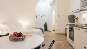 A modern kitchen with a built-in oven, a dining area with a table and chairs, and a bed with a white headboard. - VOLTA COLLECTION BY HALLDIS (Como)