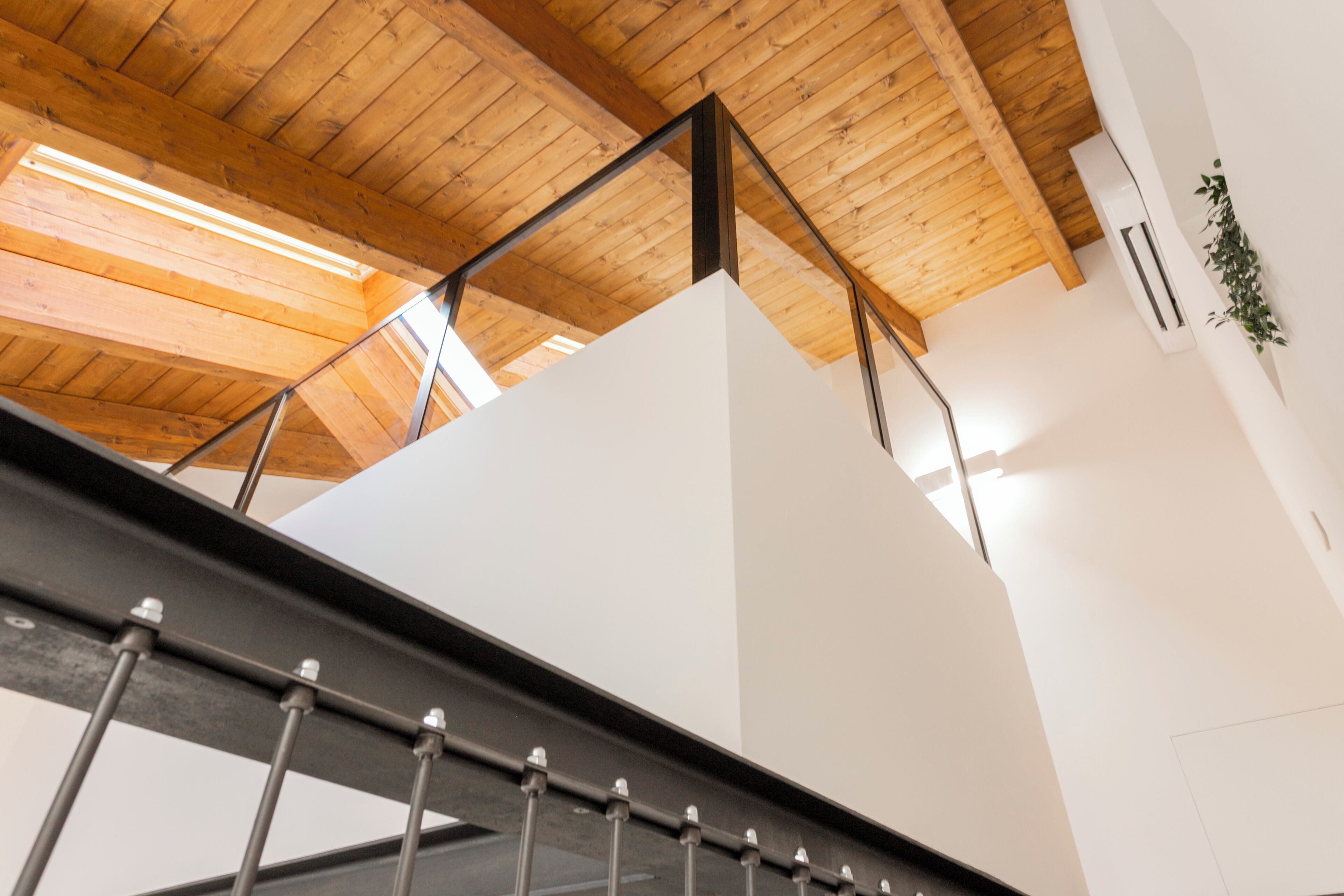 A modern interior with wooden beams, a metal staircase, and a white wall with an air conditioning unit.