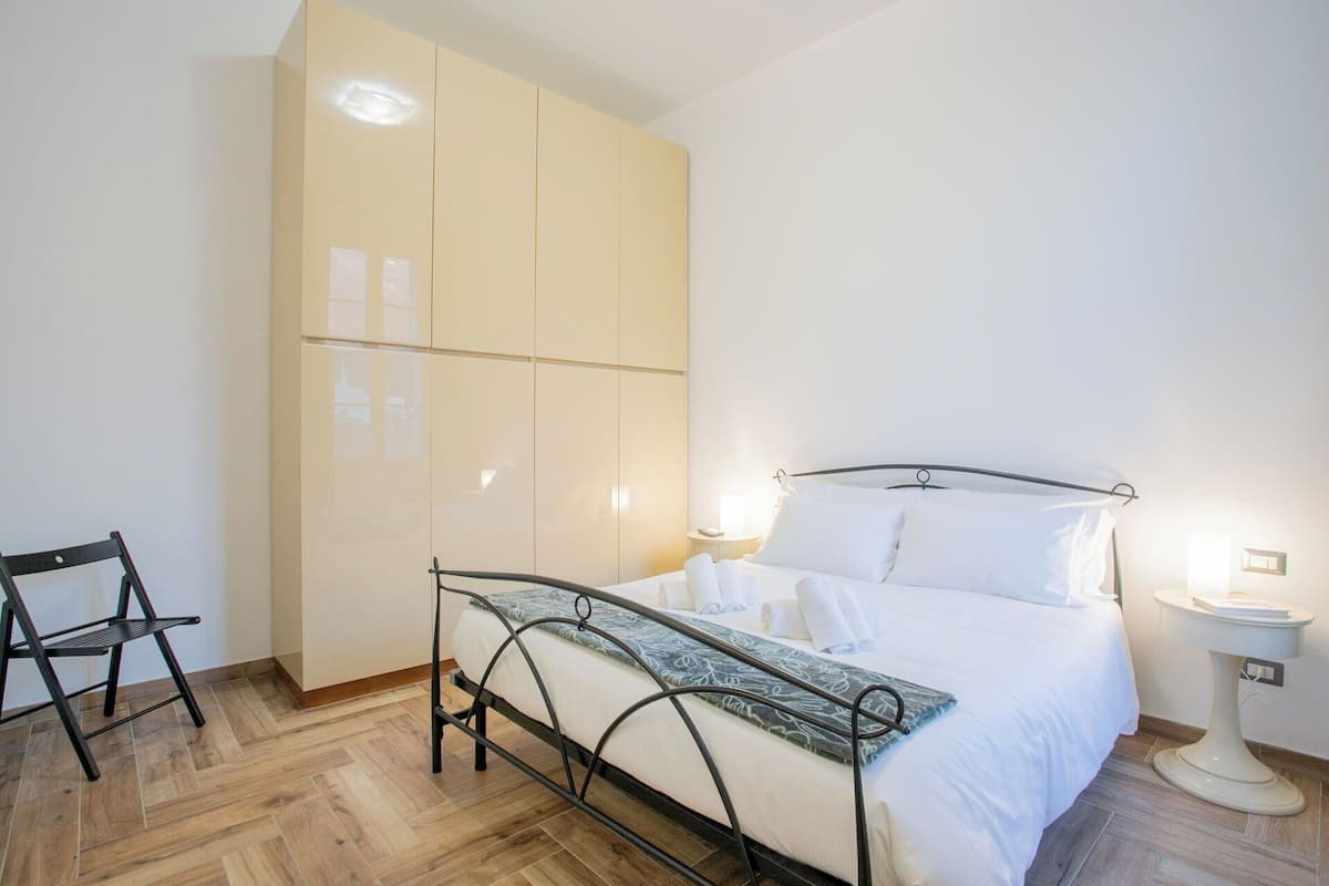 A bedroom with a bed, a wardrobe, a chair, and a bedside table.