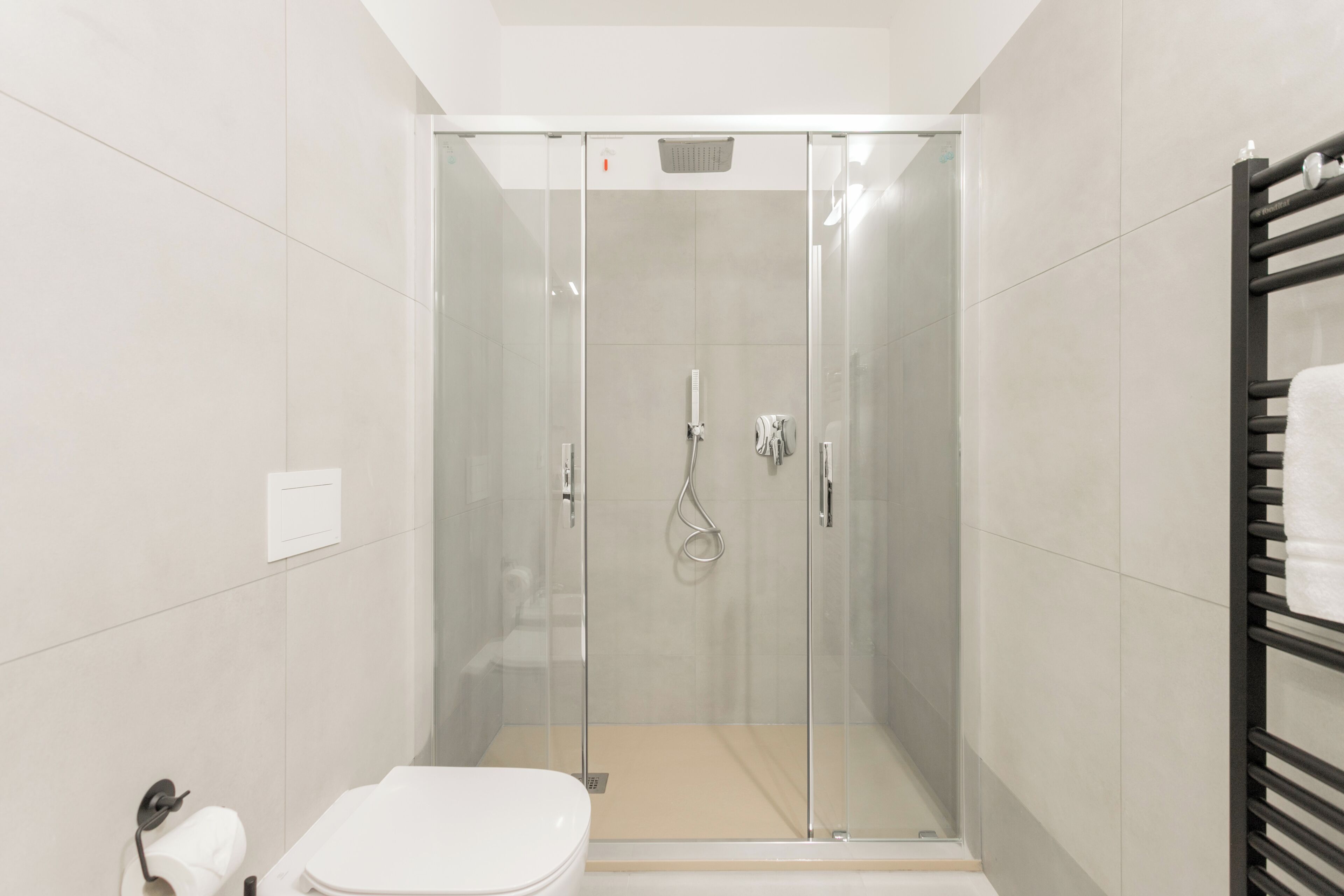 A modern bathroom with a glass-enclosed shower, a white toilet, and a black towel rack.