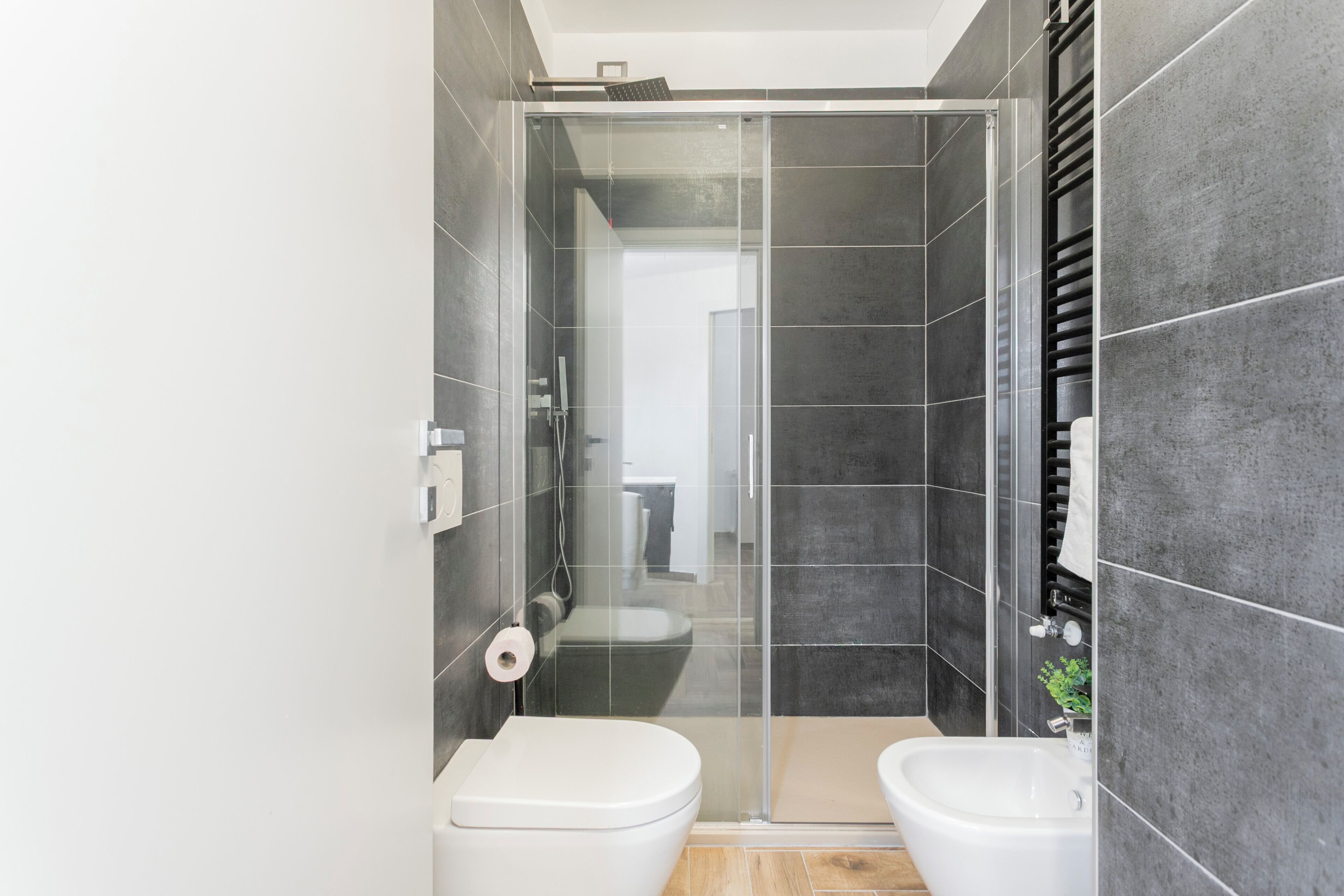 A modern bathroom with a glass-enclosed shower, two toilets, and a bidet.