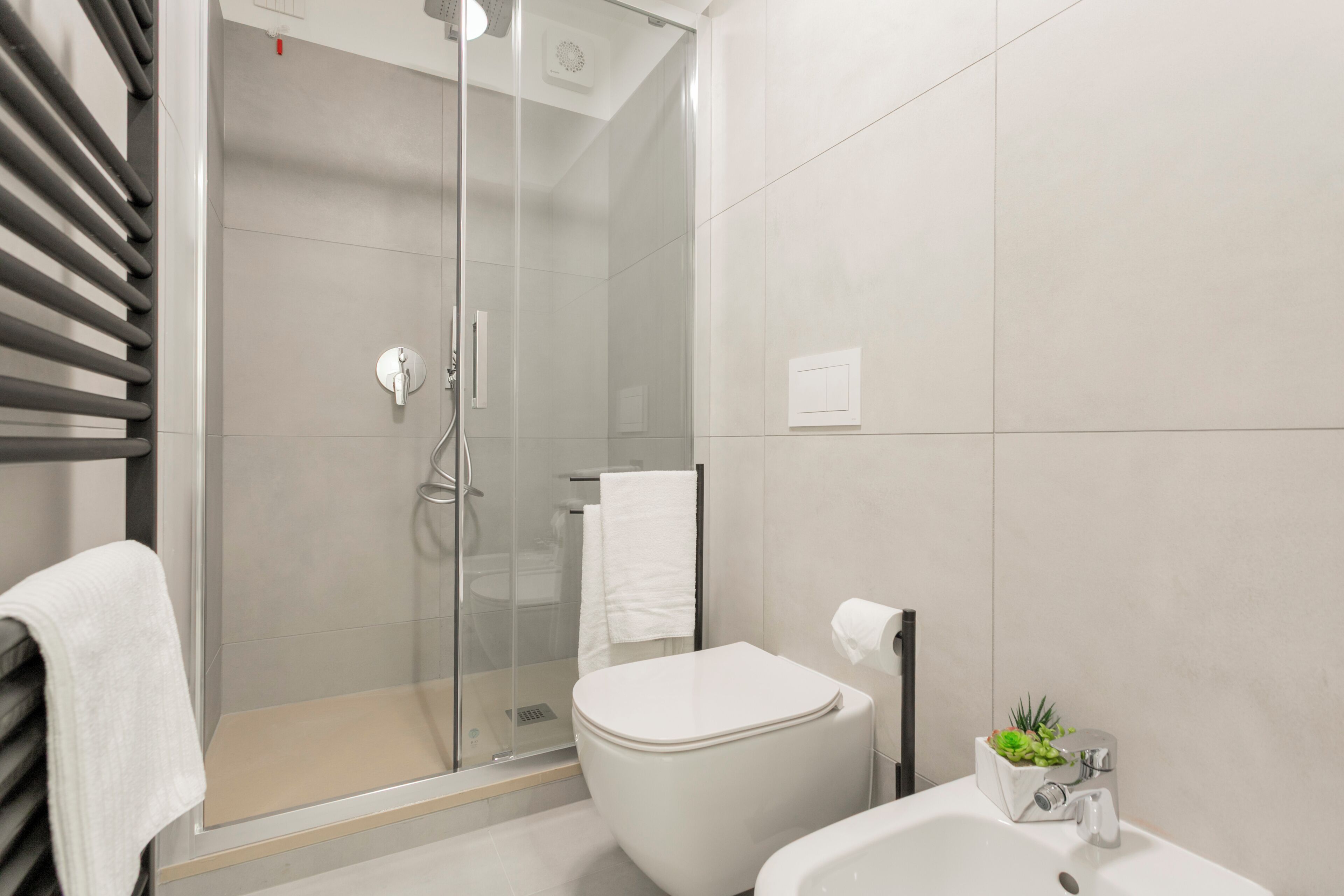 Une salle de bain moderne avec une douche à parois de verre, des toilettes blanches et un lavabo agrémenté d’une plante.