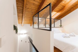 Une chambre avec un plafond en bois, un lit recouvert de draps blancs et une petite plante accrochée au mur.