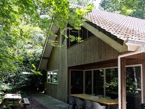 A wooden house with a sloped roof, large windows, and a patio area with a table and chairs. - House in the Woods in Drenthe (Een)