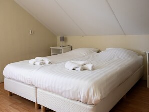 A neatly made bed with two rolled towels, a bedside table with a lamp, and a small nightstand. - House in the Woods in Drenthe (Een)