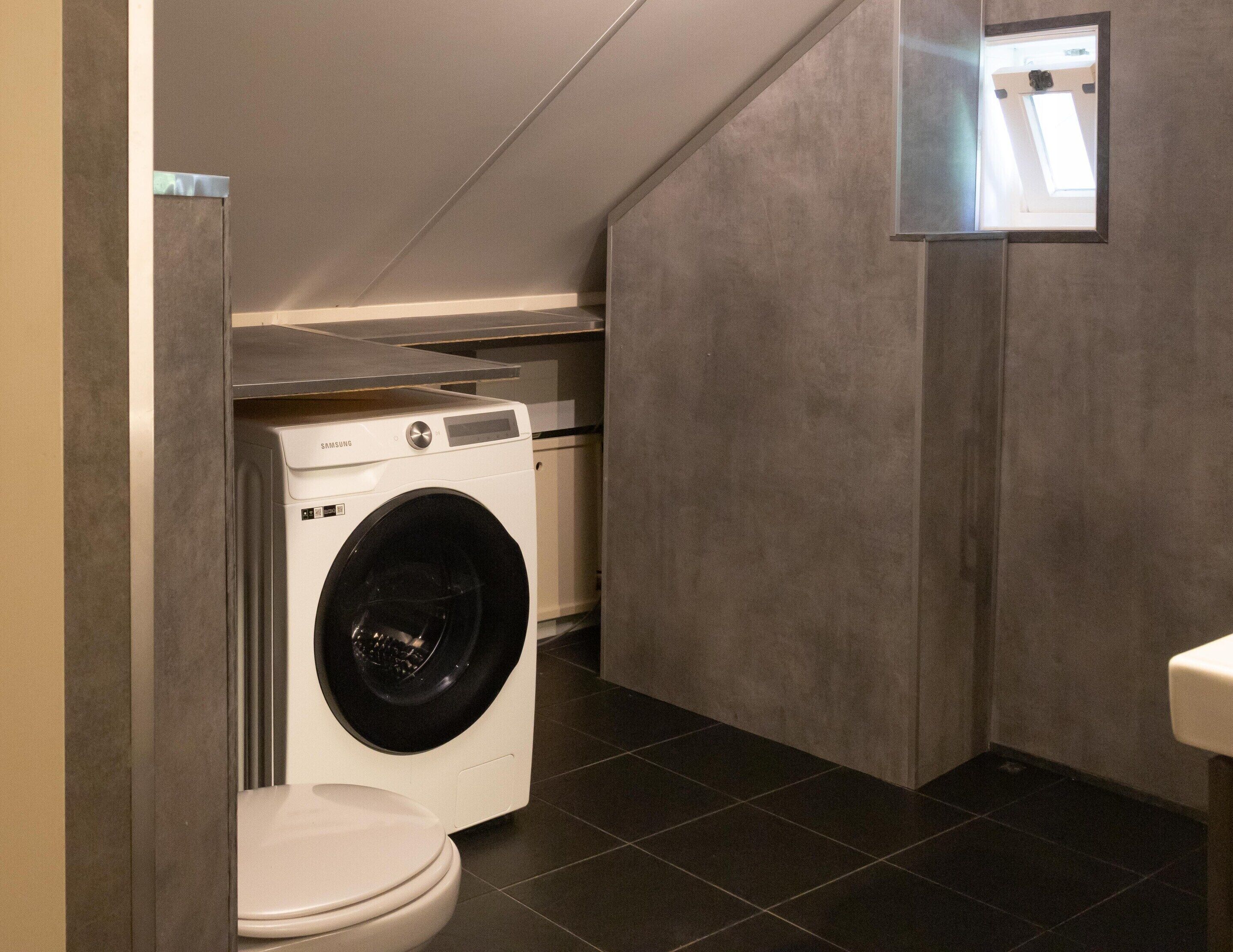 Een kleine badkamer met een wasmachine, toilet en een klein raam.