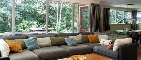 A modern living room with a sectional sofa, a wooden coffee table, and large windows offering a view of the outdoors.