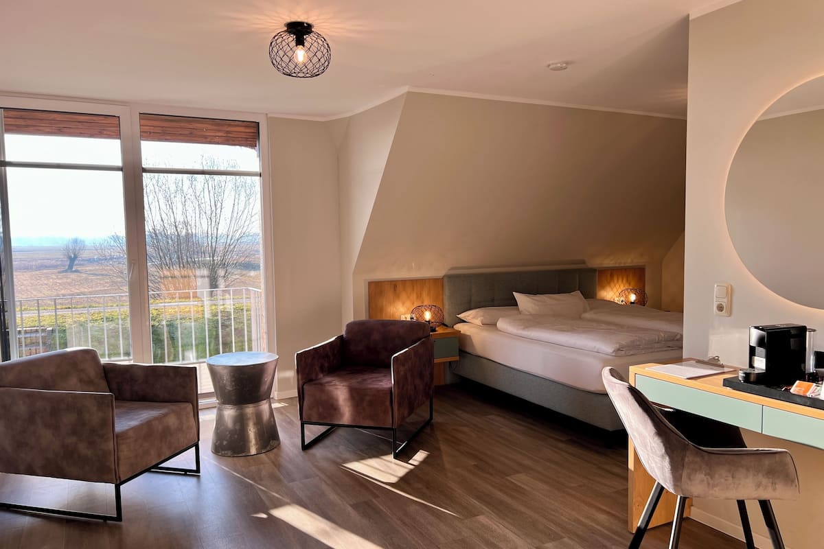 A modern bedroom with a bed, bedside table, chair, desk, and a view of the outdoors.