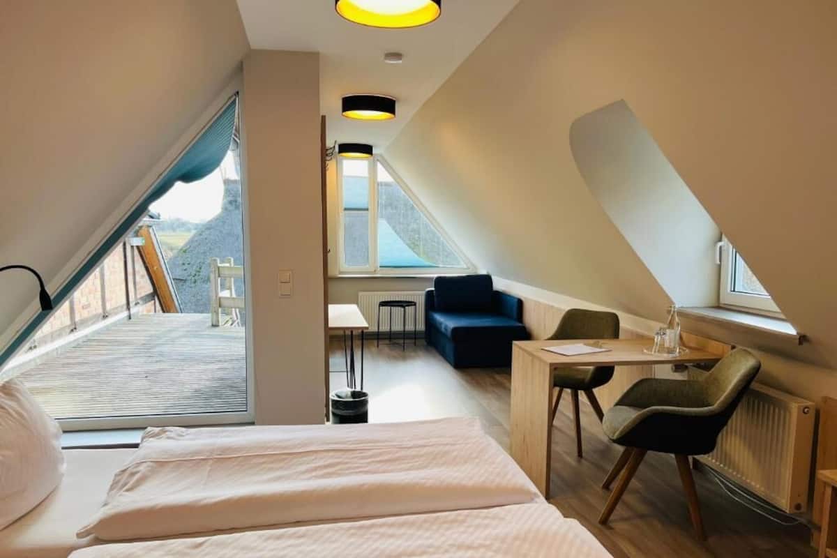 A modern bedroom with a large bed, a desk, and a chair, with a view of the outdoors.