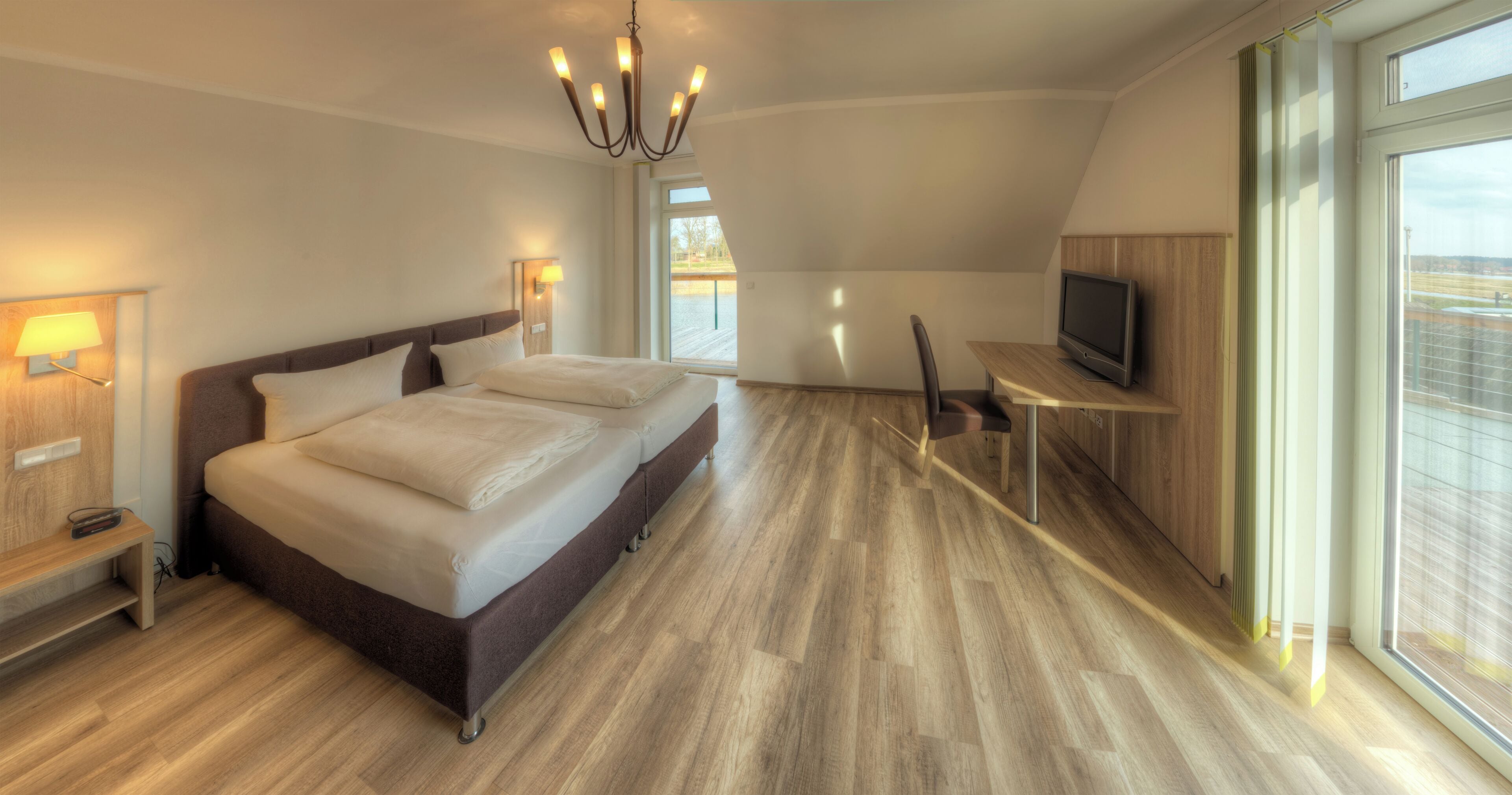 Quarto de hotel moderno com uma cama grande, televisão, escrivaninha e vista para o exterior.