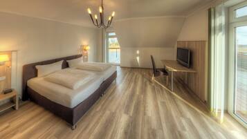 Quarto de hotel moderno com uma cama grande, televisão, escrivaninha e vista para o exterior.