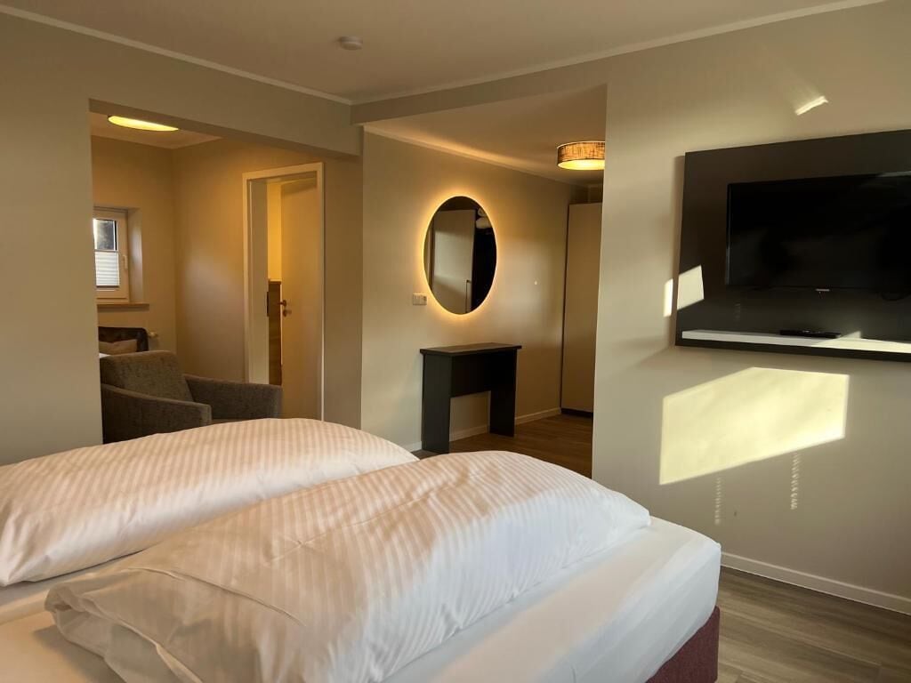 Habitación de hotel con cama, televisor montado en la pared, espejo y una mesita.