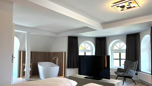 A modern hotel room with two beds, a bathtub, a flat-screen TV, and large windows with curtains. - Hotel Alte Fischerkate (Lenzerwische)