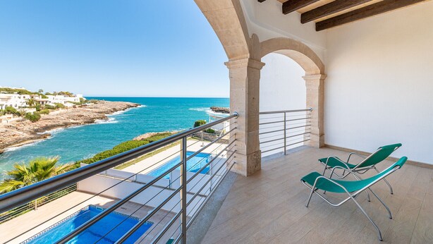 Un balcon avec vue sur la mer, une piscine et deux chaises vertes.