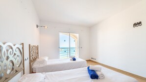 Une chambre d’hôtel avec deux lits, un balcon donnant sur la mer et une décoration aux tons blancs.