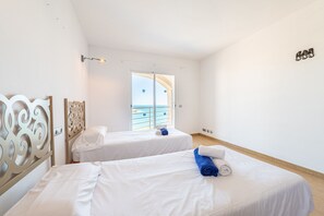 Habitació d'hotel amb dos llits, un balcó i vistes al mar, amb una decoració de tons blancs.