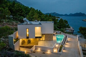 Ein modernes Haus mit Swimmingpool, umgeben von Bäumen und mit Blick auf ein Gewässer.