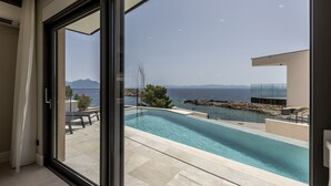 Een moderne villa met een privé-oneindig zwembad met uitzicht op een rotsachtige kustlijn en de zee.