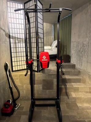 Una barra para dominadas con pomos rojos, un colchón y una ventana con un diseño de celosía.