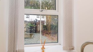 A bathroom with a large window, a wooden door, and a bamboo reed diffuser. - Bobtail Cottage (Kendal)