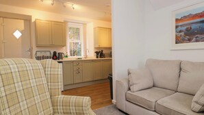 A living room with a sofa and armchair, a kitchen with cabinets and a window, and a painting on the wall. - Bobtail Cottage (Kendal)