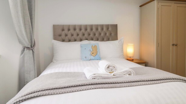 A neatly made bed with a pillow featuring a cartoon character, a bedside lamp, and a wardrobe. - Bobtail Cottage (Kendal)