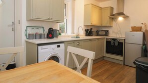 A compact kitchen with a washing machine, microwave, and a small refrigerator. - Bobtail Cottage (Kendal)