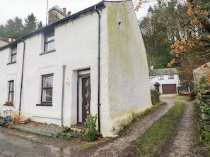 A white house with a brown door, a small porch, and a garden. - Bobtail Cottage (Kendal)