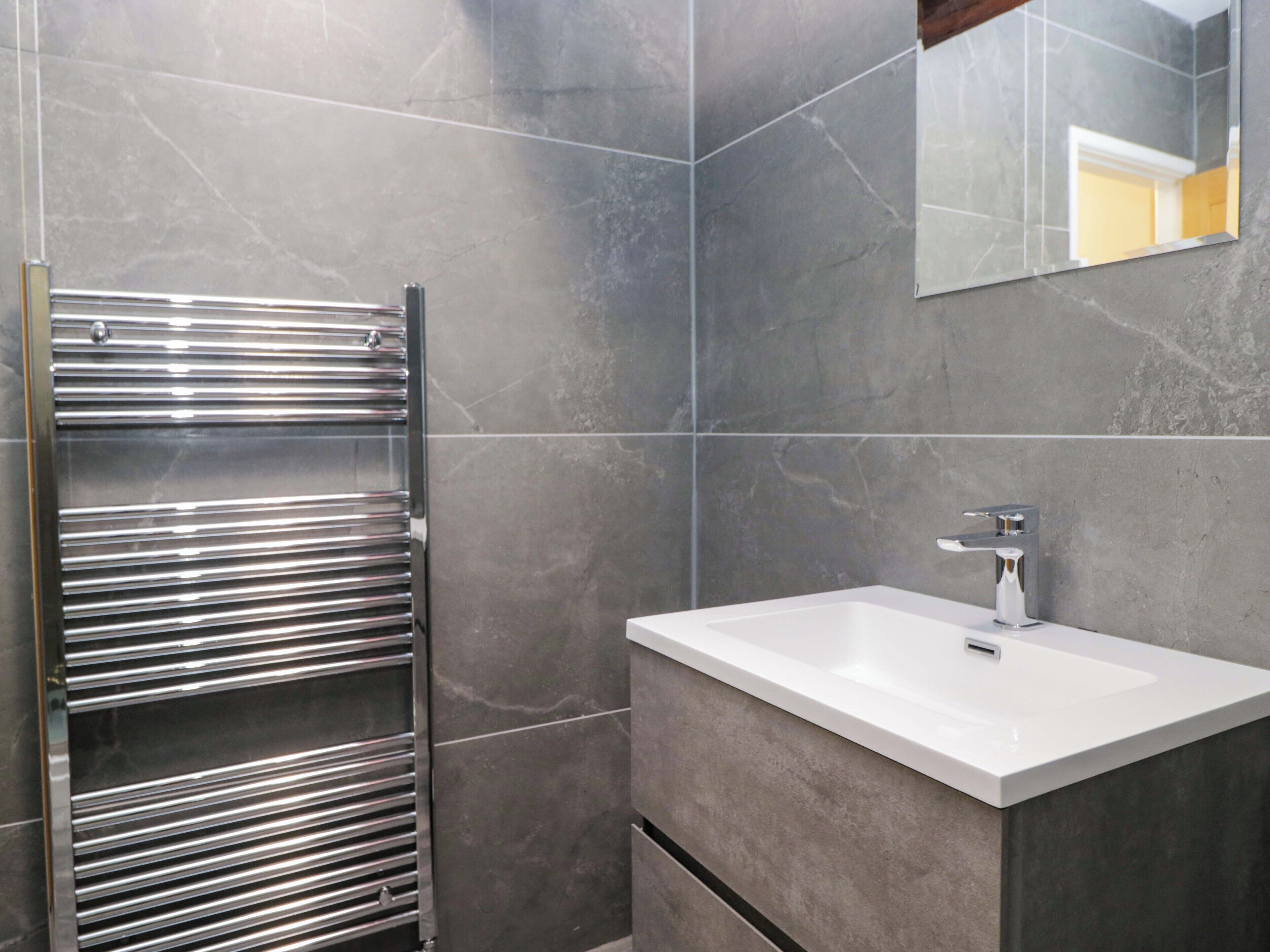 A modern bathroom with a chrome towel rack, a white sink, and a large mirror.