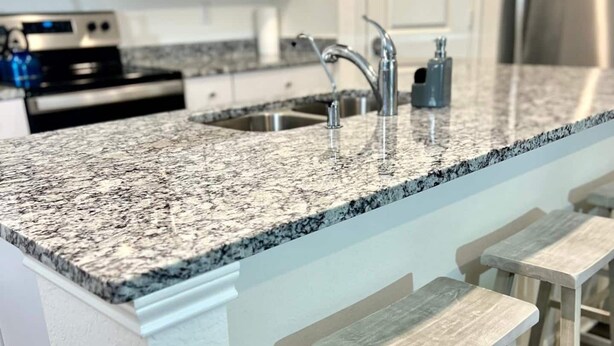 Eine Küche mit Granit Arbeitsplatte, Edelstahlgeräten und hölzernen Barhocker.