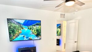 Ein Schlafzimmer mit einem Bett, einem an der Wand montierten Fernseher und einem Deckenventilator.