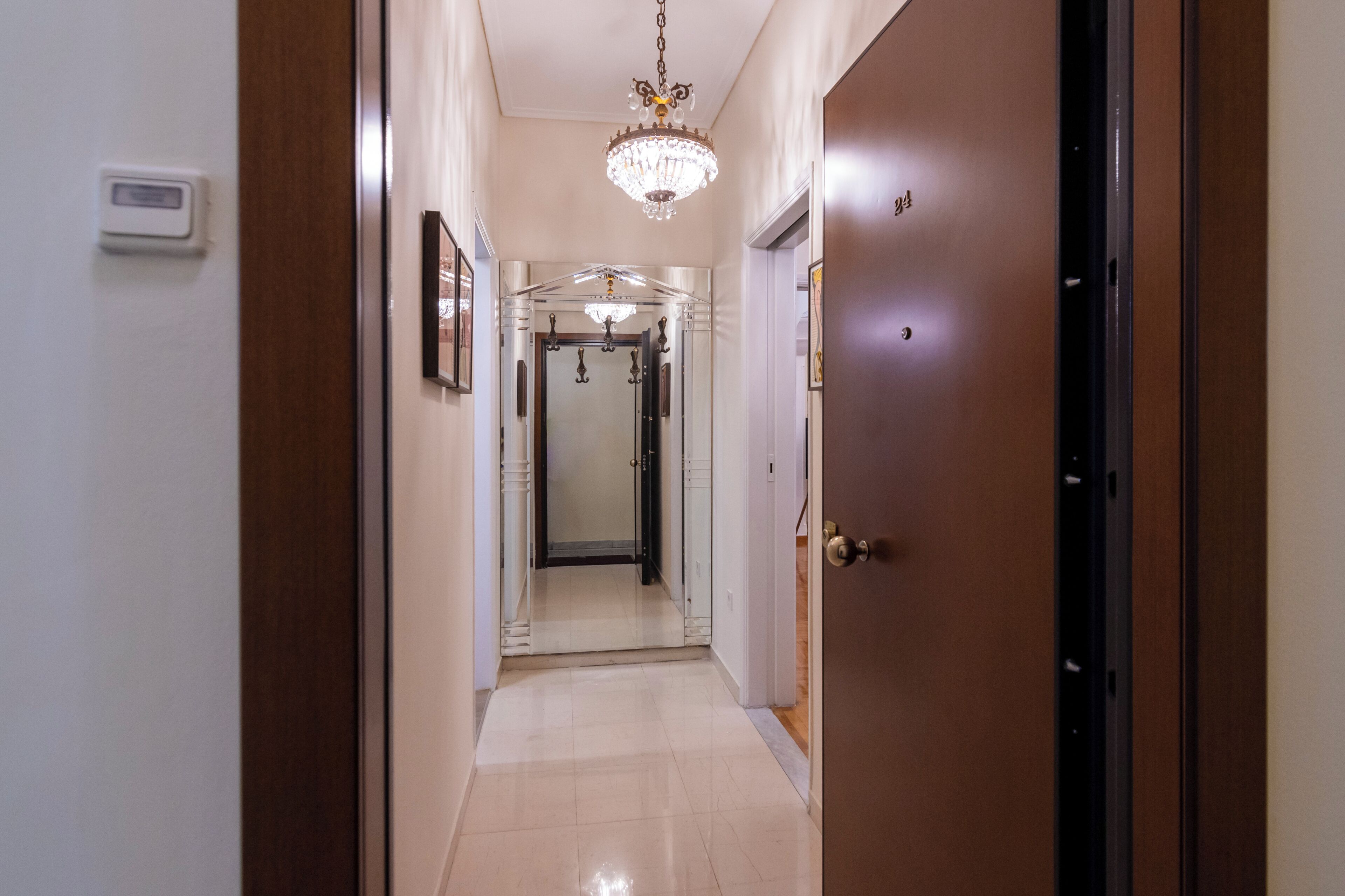 A hallway with a chandelier, a door, and a mirror.