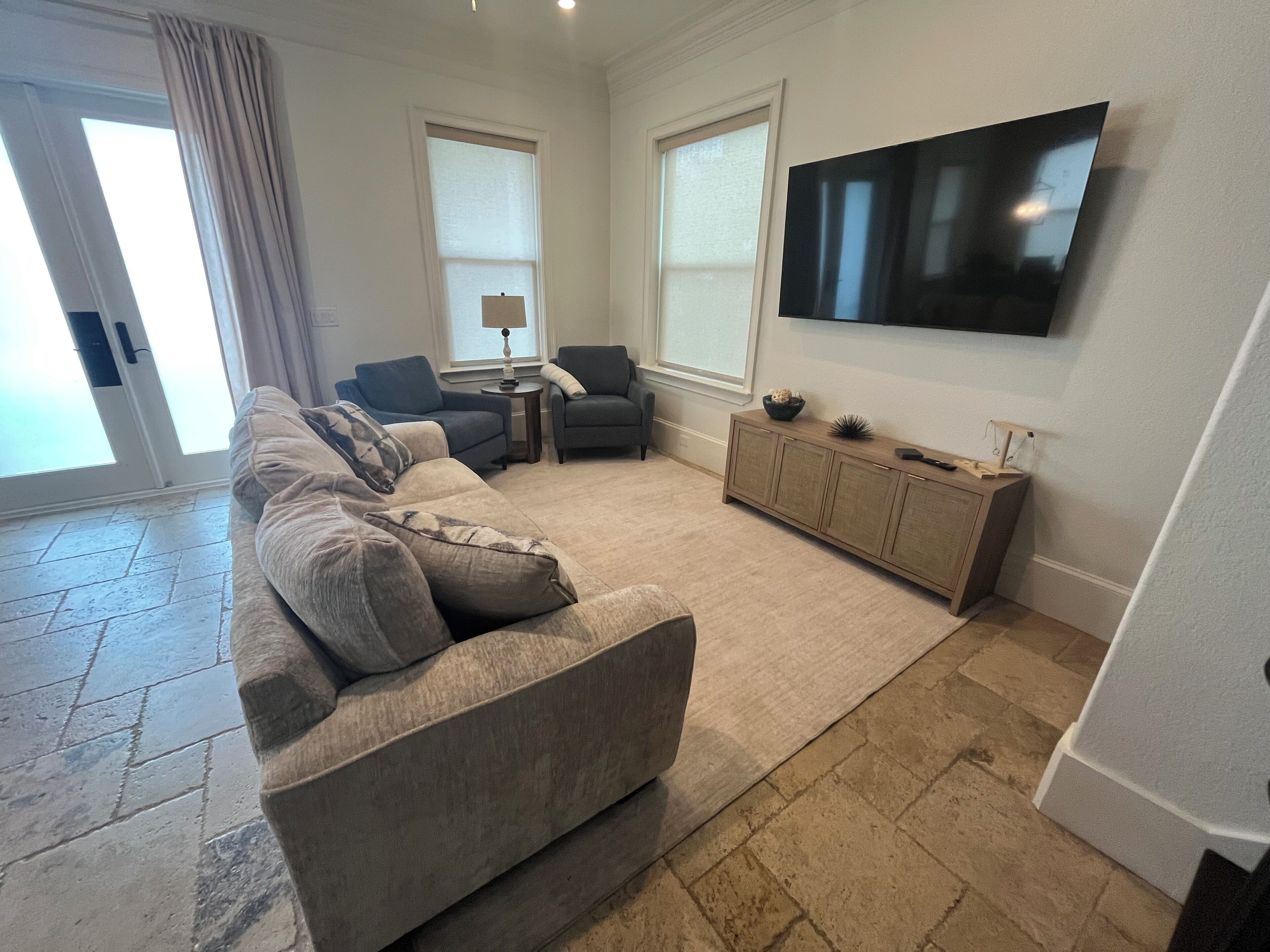 A living room with a sectional sofa, a TV mounted on the wall, and a small side table.