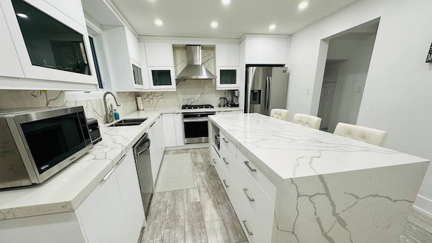 A modern kitchen with white cabinetry, a marble island, a built-in microwave, a stove, and a refrigerator. - Cozy Modern 3BR With Free Parking Fast Wifi (Richmond Hill)
