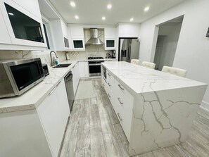 A modern kitchen with white cabinetry, a marble island, a built-in microwave, a stove, and a refrigerator. - Cozy Modern 3BR With Free Parking Fast Wifi (Richmond Hill)