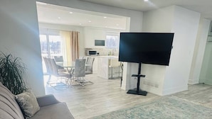 A modern living room with a sofa, a flat-screen TV, and a kitchen area in the background. - Cozy Modern 3BR With Free Parking Fast Wifi (Richmond Hill)